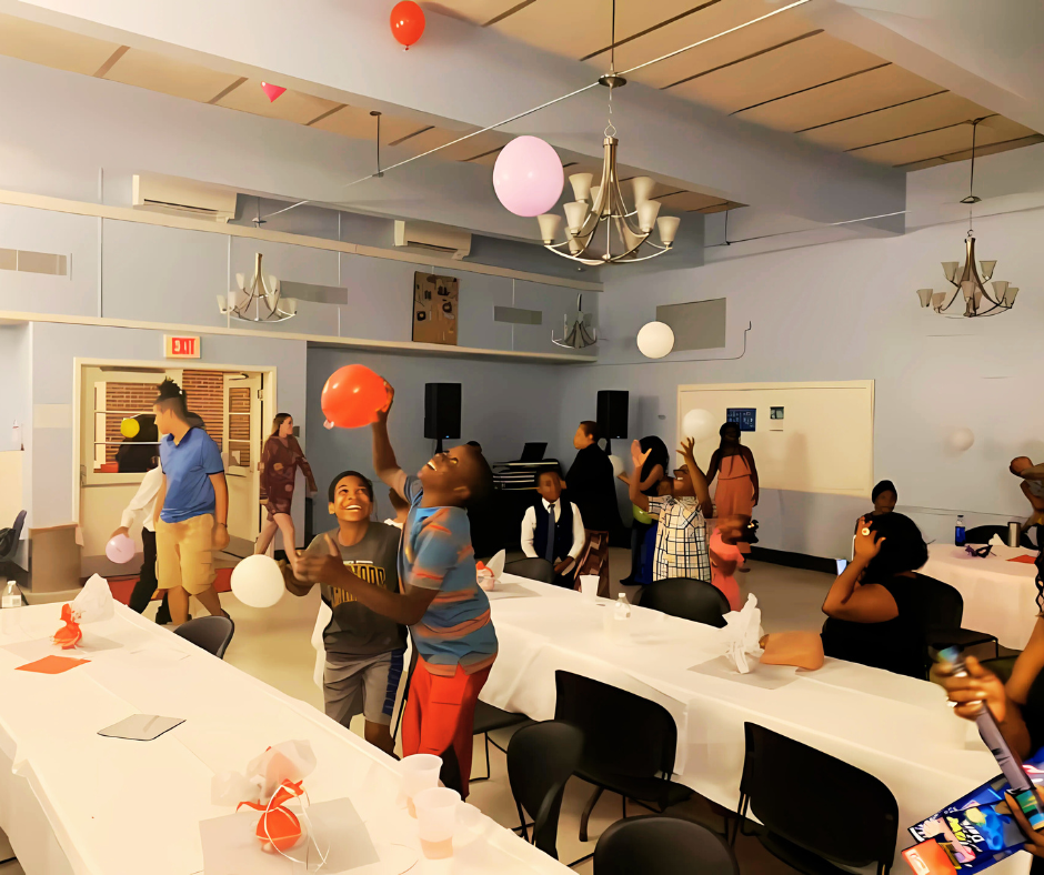 Children and adults playing with balloons in a decorated community room.