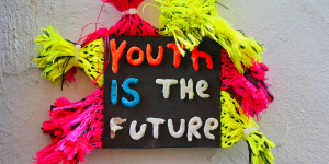 Colorful handmade sign reading “Youth is the Future” with bright tassels.