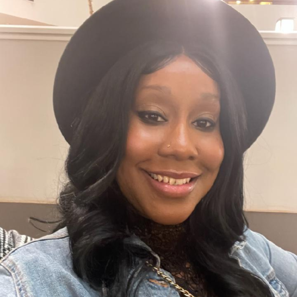 Keisha Pettaway smiling while wearing a black hat and denim jacket.